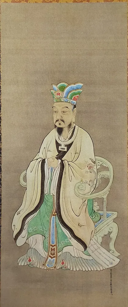 江戸時代の絵師が描いた孔子の肖像画。冠をかぶり、白い衣を着た孔子が、ひじかけのある椅子の前に立っている