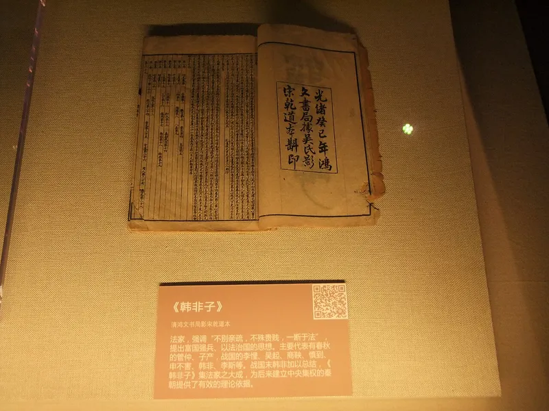 ガラスケースに展示された、開いた古い和とじの本と説明の札